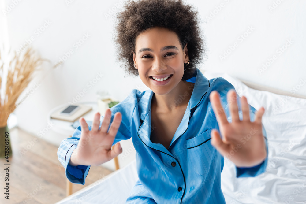 happy african american woman in pajamas gesturing while sitting on bed happy african american woman in pajamas gesturing while sitting on bed