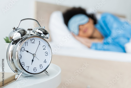 alarm clock near blurred african american woman in bed