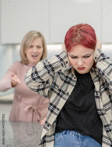 Angry mother scolds her teen daughter. Girl covers her ears and ignores her mother. Family relationships concept