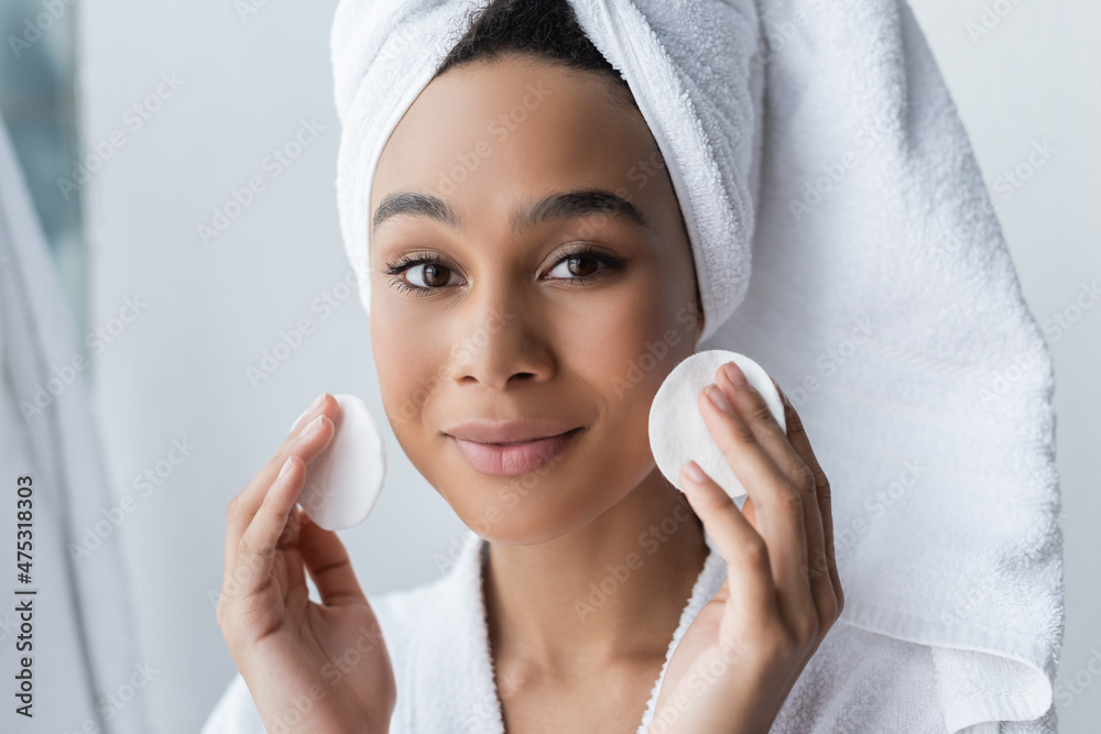 smiling african american woman in towel holding cotton pads in bathroom