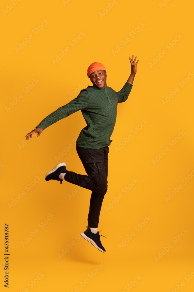 Cheerful Excited Black Hipster Guy Jumping In Air Over Yellow Background
