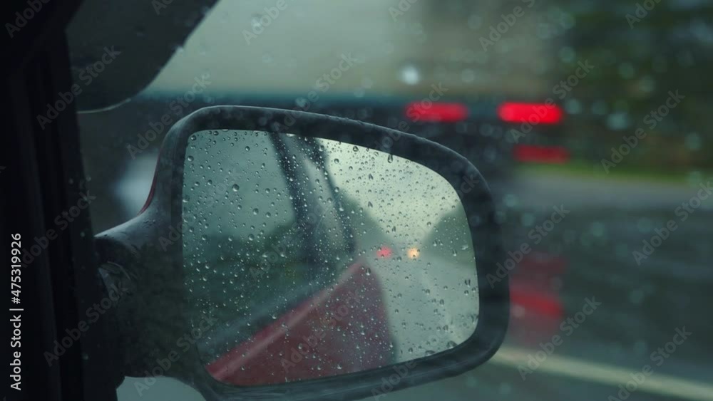 Rain Drops on Rearview Mirror Reflection of Road. Landscape with empty highway going through the Green Autumn Forest. Car speeding. Auto in motion. Tourism, travel, trip concept. Fresh new herbs.