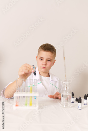 a white boy in a white coat conducts a chemical experiment. The boy prepares paints