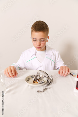 A boy in a white coat looks at the result of a chemical experiment
