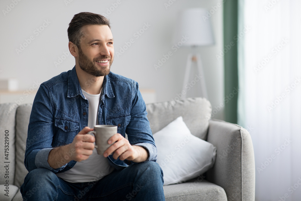 Cheerful bearded man enjoying cup of coffee at home