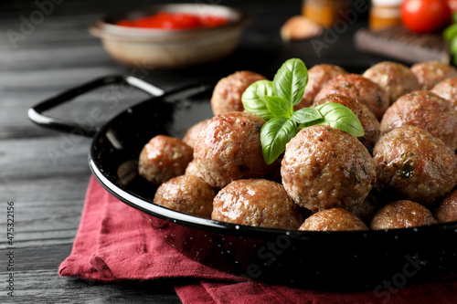 Tasty cooked meatballs with basil on black wooden table, closeup