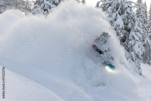elite sports snowmobiler rides and jumps on steep mountain slope with swirls of snow storm. a trail of splashes of white snow. bright snowmobile and suit without brands
