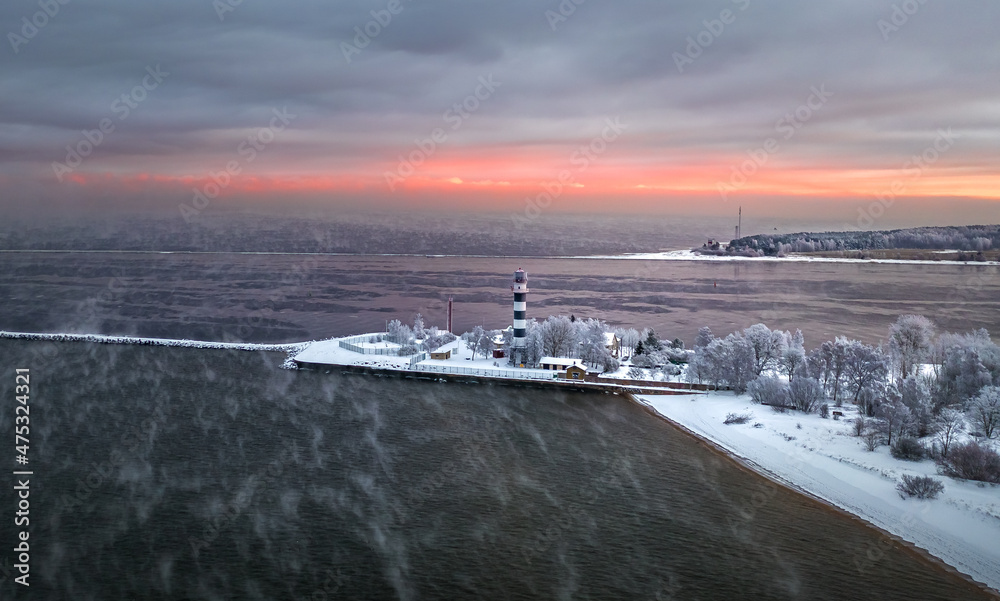 Breakwater leading into Baltic sea at winter. Sea covered in fog and ice blocks. Beautiful lighthouse at sunrise.
