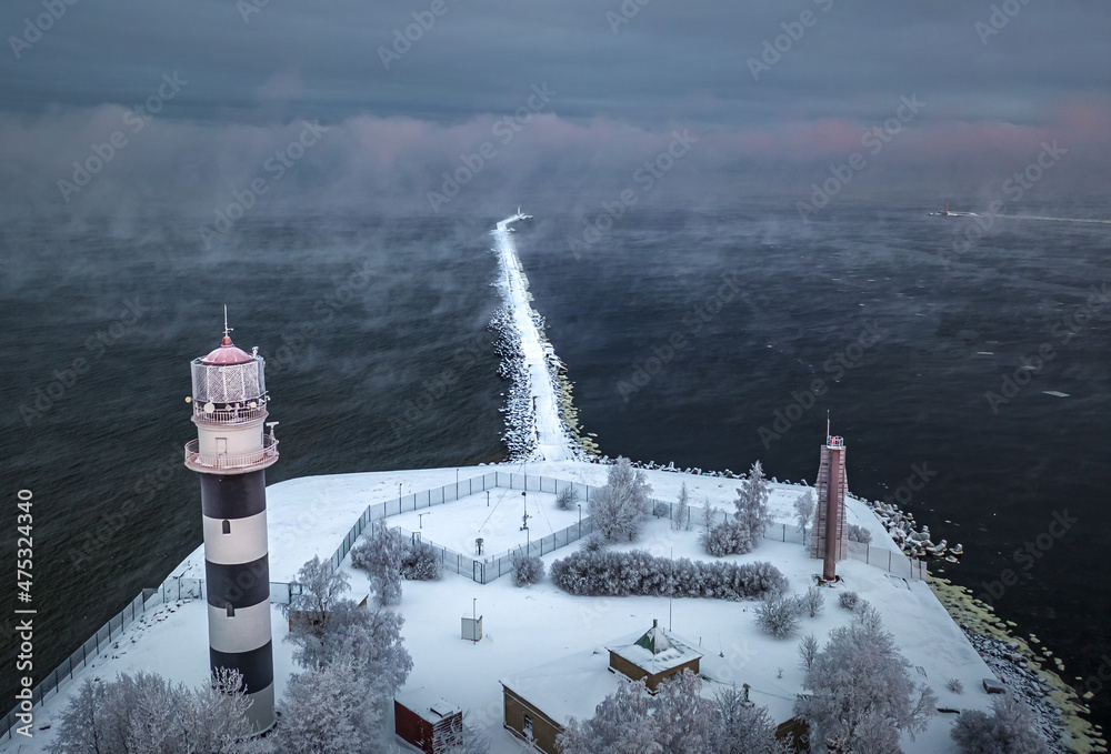 Breakwater leading into Baltic sea at winter. Sea covered in fog and ice blocks. Beautiful lighthouse at sunrise.