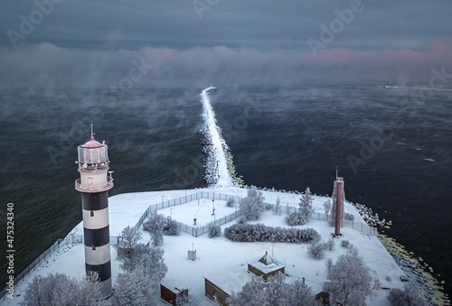Obraz na płótnie Breakwater leading into Baltic sea at winter. Sea covered in fog and ice blocks. Beautiful lighthouse at sunrise. w salonie