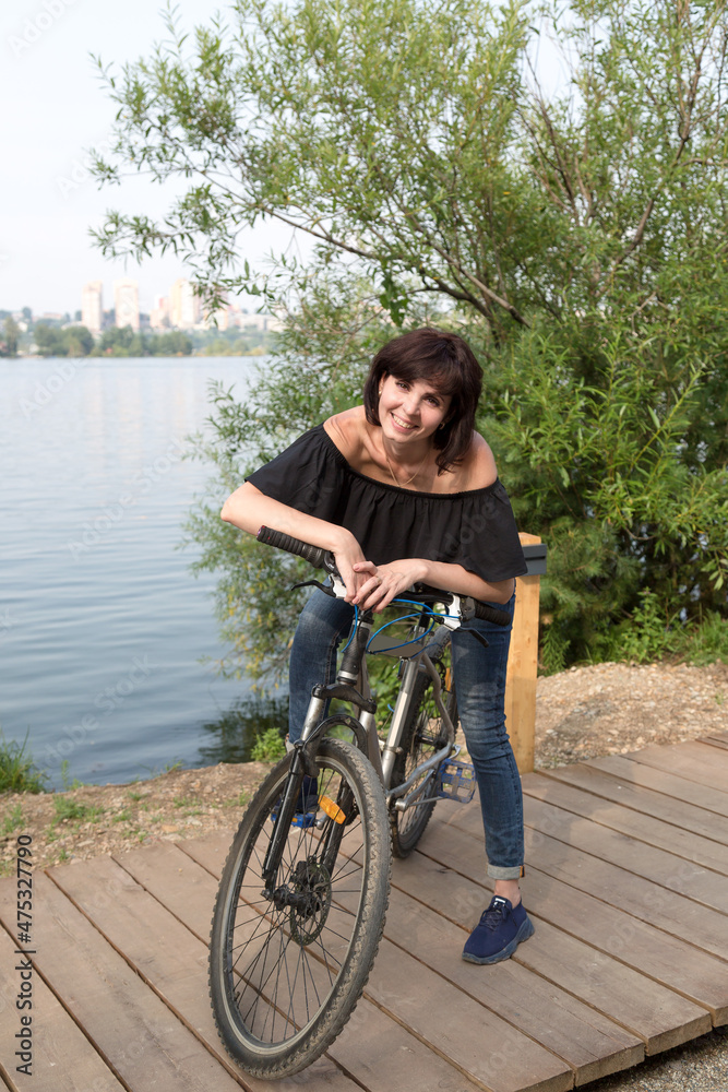 Obraz premium The smiling brunette stopped rest on the riverbank while riding a bike.