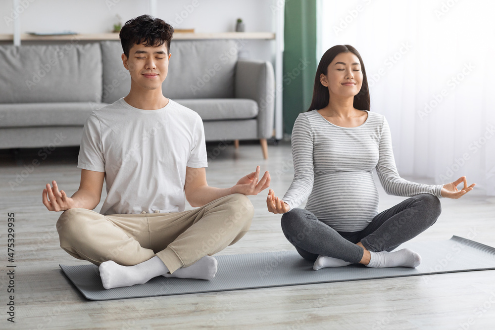 Relaxed expecting asian couple having yoga practice together