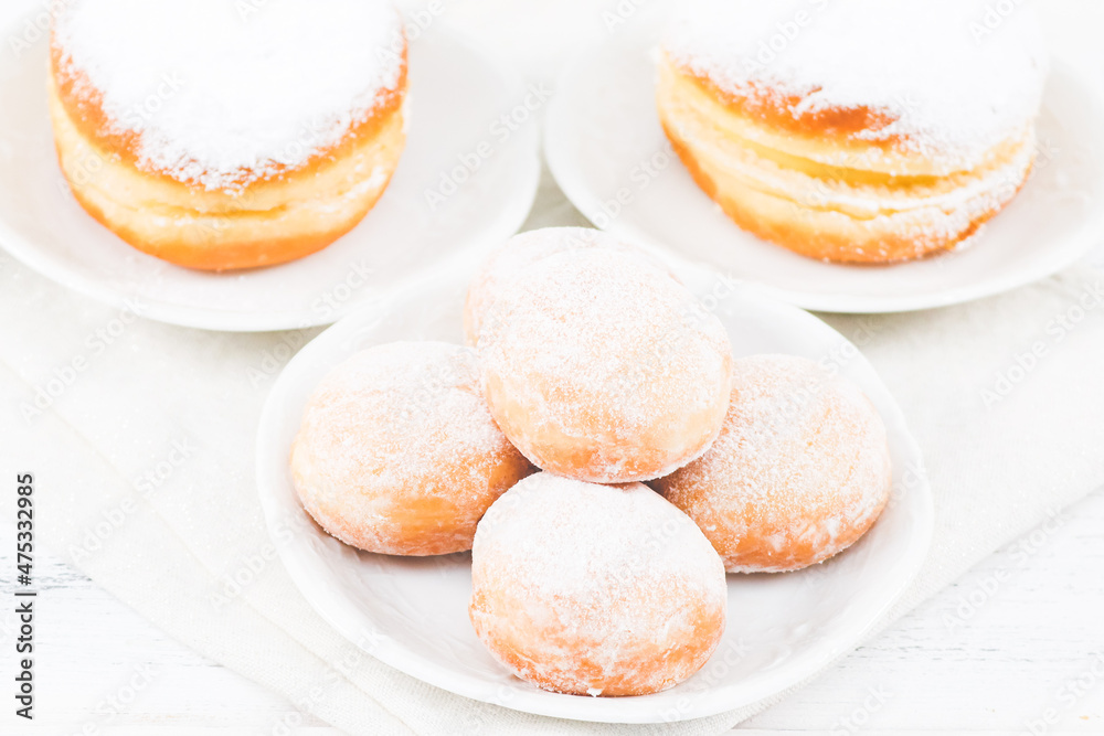 Donuts with powdered sugar and cream in saucers with a kitchen napkin on a white wooden table.