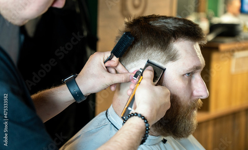 Close up view of the bearded man in barbershop taking care of his beard. Side view of handsome bearded man having his beard cut by hairdresser at the barbershop