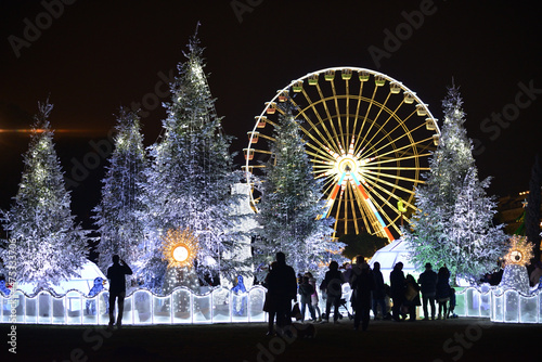 People watch Christmas decorations with snow-covered trees and funfair Ferris wheel. Nice, France
