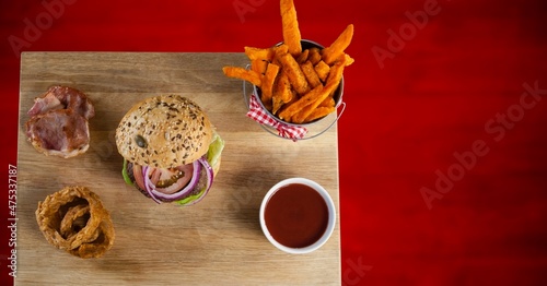 Overhead view of fast food on a wooden tray against red background