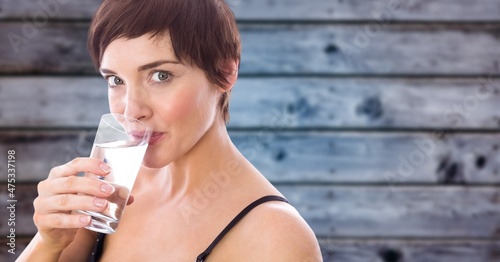 Composite image of caucasian woman drinking water from a glass against wooden background
