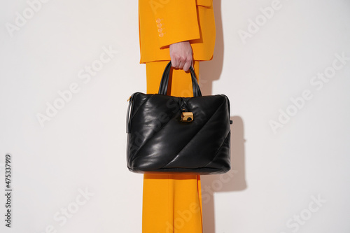 Woman in an orange suit with black leather handbag in her hand on the white background. Quilted tote bag stylish accessory. New collection or sale background. Horizontal photo with copy space.
