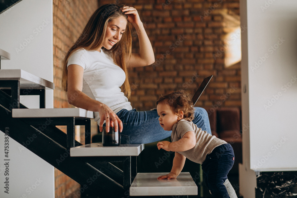 Obraz premium Young mother working from home on laptop with her little son