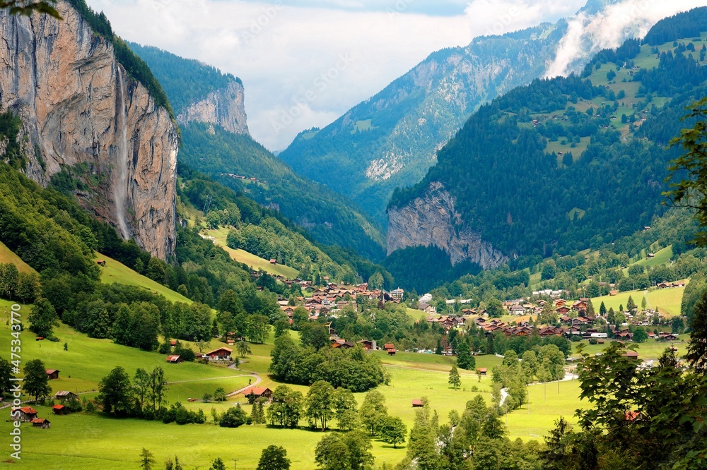Summer scenery of beautiful Lauterbrunnen village with the famous Staubbach waterfall tumbling down the rocky cliff and chalet houses in the green grassy valley, in Bernese Oberland, Switzerland