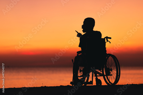 Behind of young man with disability looking sunset on the sea beach at summer, Positive photos give life energy and power concept.