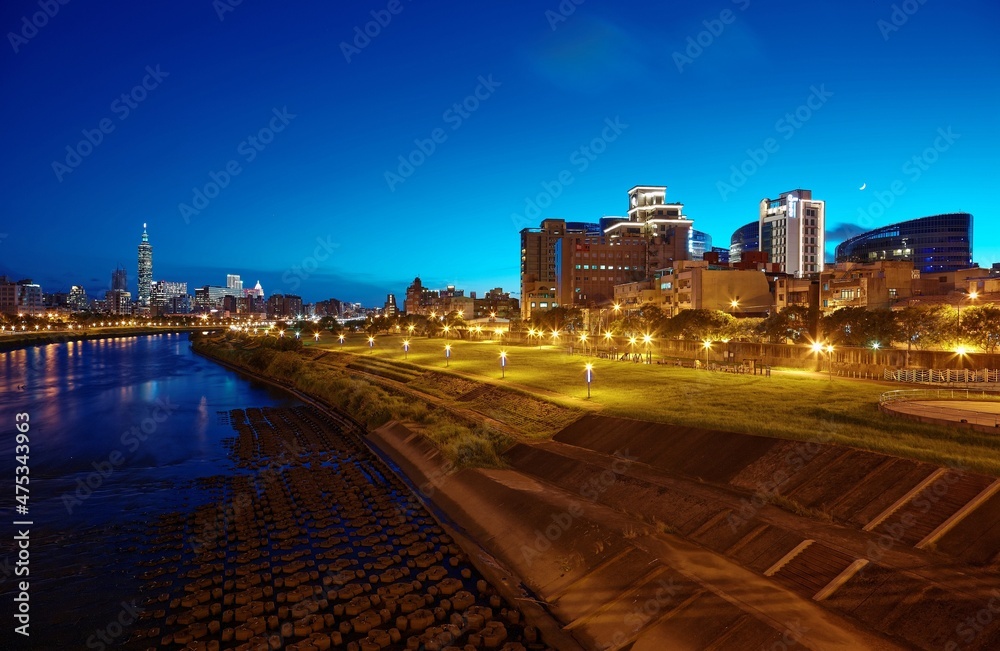 Night view of Taipei City by riverside with skyscrapers and beautiful reflections on smooth water ~ Landmarks of Taipei 101 Tower, Keelung River, Xinyi District and downtown area at dusk