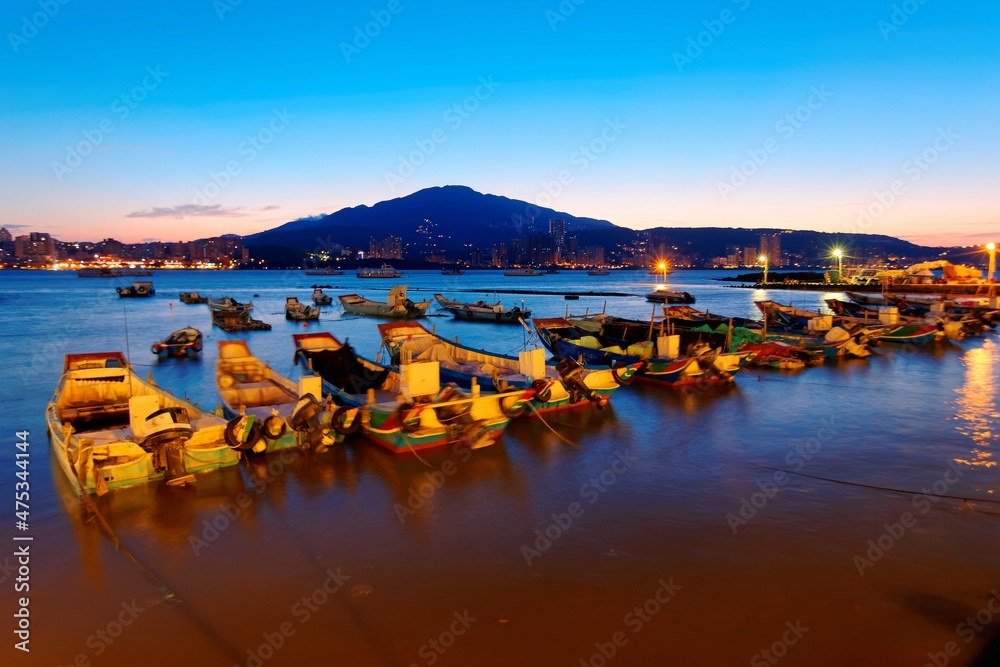 Morning scenery of Tamsui River at sunrise in Bali District, Taipei, Taiwan, with a peaceful view of ferry boats parking on the smooth water & Datun Mountain under beautiful dawning sky in background