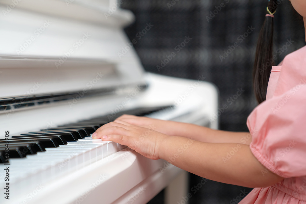Fototapeta premium Selective focus on the kid finger playing grand piano. Teacher or instructor teach a girl on the class play melody. Close up hand of child. Music with piano. Education and learning concept.