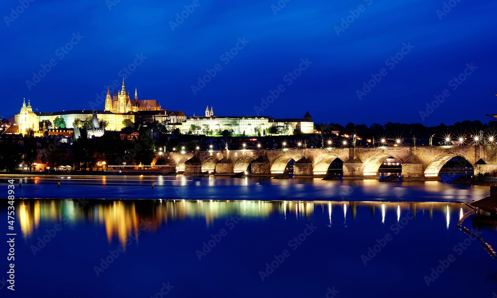 Beautiful scenery of Charles Bridge over Vltava River at blue dusk with the majestic Prague Castle & St. Vitus Cathedral in background and reflections of lights on the water, in Old Town Prague, Czech