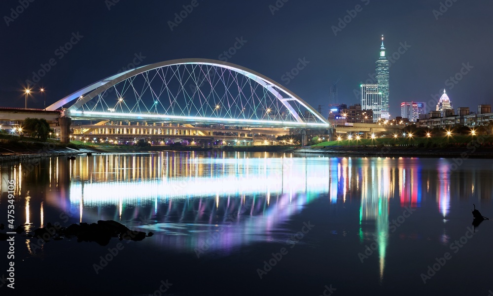 Night scenery of Taipei City with beautiful reflections of skyscrapers and bridges in the water at dusk. Cityscape of Taipei 101 Tower, Keelung River, Xinyi District and downtown in blue twilight