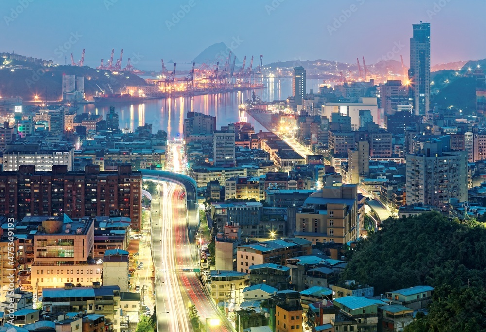 Fototapeta premium Night view of Keelung, a busy harbor city in northern Taiwan, with traffic trails on the streets at blue dusk and beautiful reflections of lights on the water in twilight