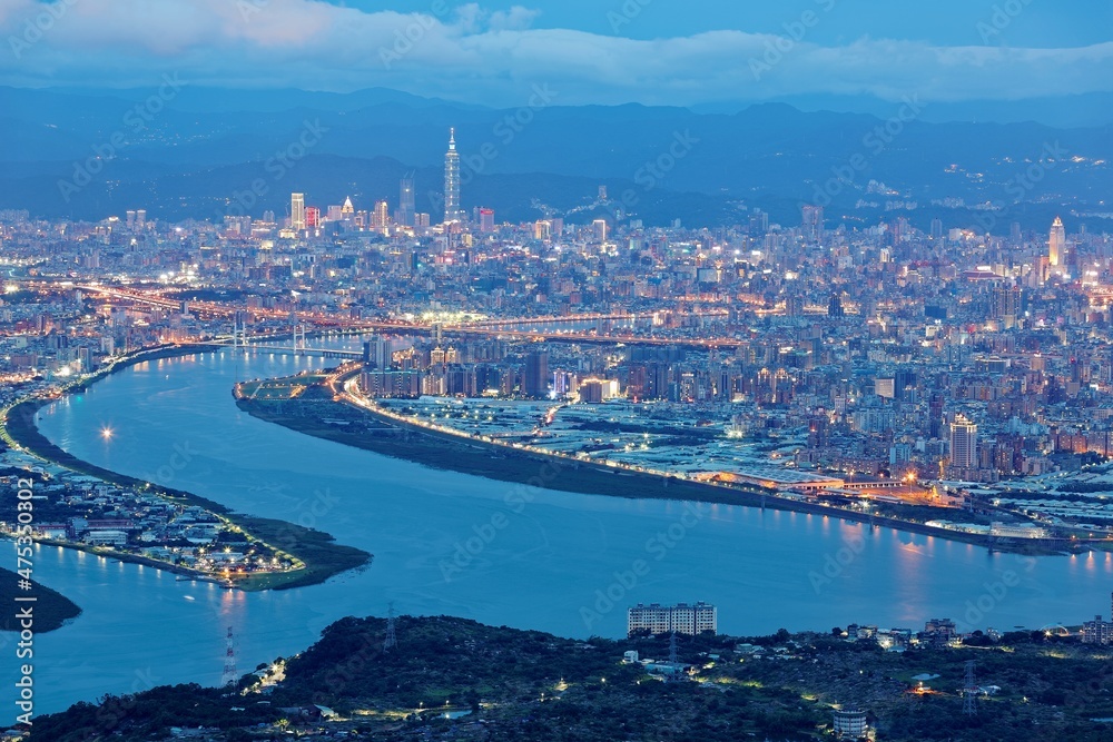 Fototapeta premium Aerial panorama over Taipei, capital City of Taiwan, on a blue gloomy evening with view of the confluence of Tamsui & Keelung River & Taipei 101 Tower among high rise skyscrapers in Downtown at dusk