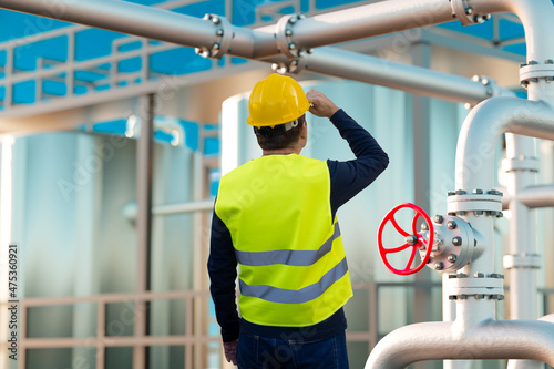 A worker in a helmet and a yellow vest next to a valve against the background of an oil and gas terminal as a concept of an industrial background photo