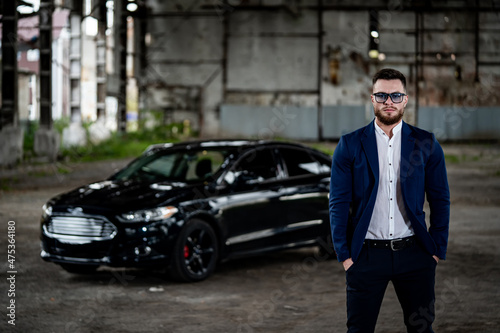 Stylish handsome man with sunglasses in fashionable clothes standing with the luxury black car on the background. Closeup © Vadim