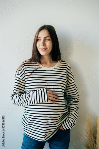 Vertical portrait of a young pregnant woman in a striped sweatshirt.