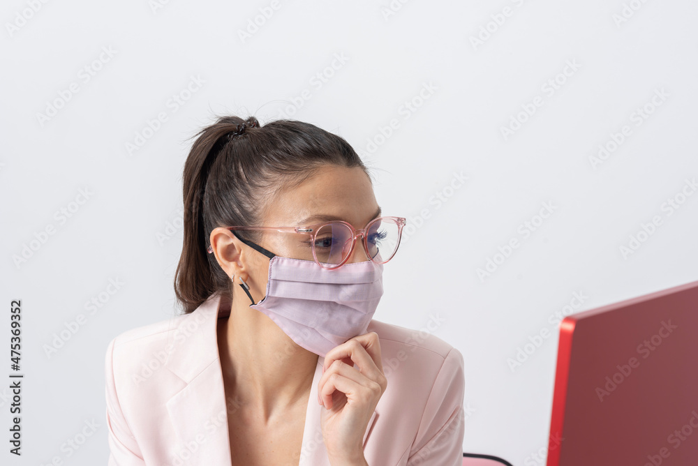 Salisbury, Wiltshire, UK. 2021. Attractive woman wearing pink face mask and looking at a computer screen. Salisbury, Wiltshire, UK. 2021. Attractive woman wearing pink face mask and looking at a computer screen.