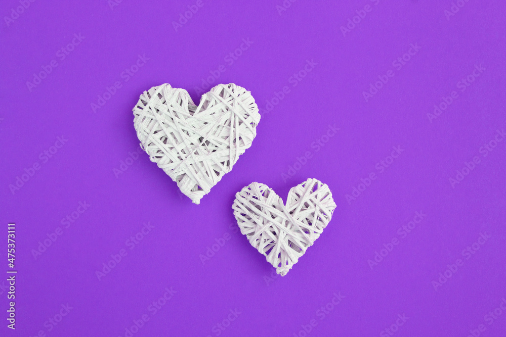 Top view of  two white braided hearts on the purple background. Copy space. Close-up.