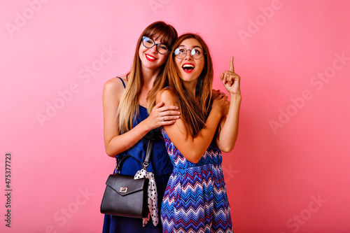 Two exited pretty women posing at pink background