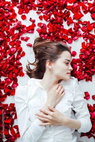 a beautiful woman lies in the flowers of the petals of red roses