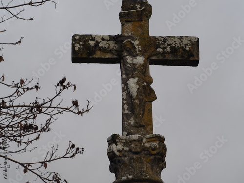 cruz de granito gris con la imágen de jesús crucifica, enseñando las palmas de las manos , sobre un capitel donde se observa la escultura de un rostro, mellid, la coruña, españa, europa  photo