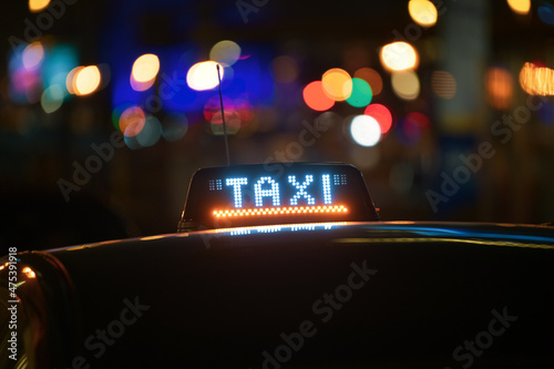 Taxi sign on top of a taximetre car in Brussels, Belgium. Photo shot during the night with city lights in background.