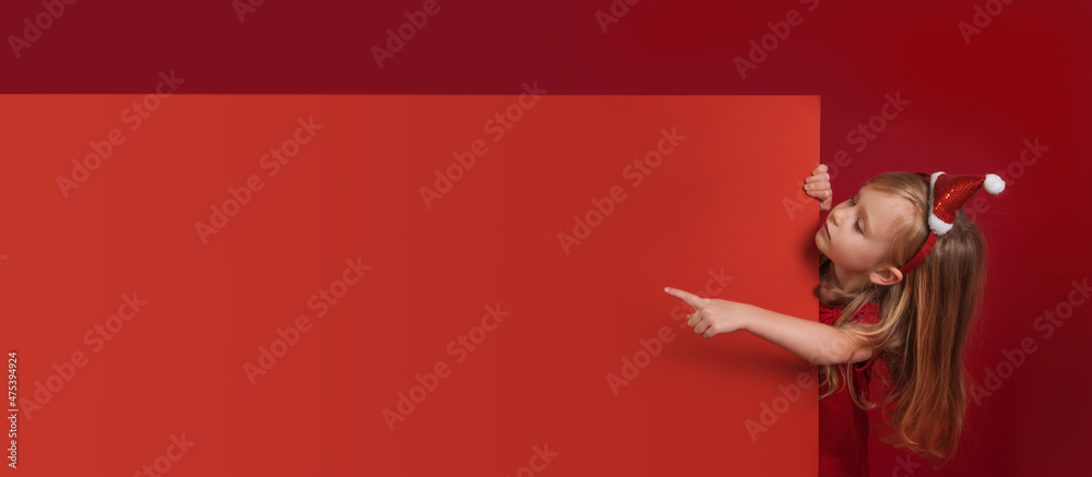 Girl in Christmas clothes points to big blank red banner, copy space for design Girl in Christmas clothes points to big blank red banner, copy space for design
