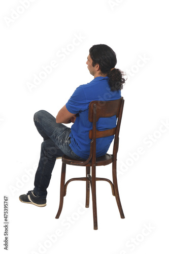 rear  and side view of aman with ponytail and casual clothing  sitting a chair legs and arms crossed on white background