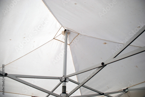An iron structure supporting the tarpaulin canopy. A metal structure of various rails and joints holds a white tarpaulin awning in the form of quadrangular primaids.