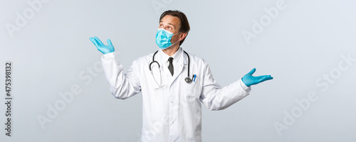 Covid-19, preventing virus, healthcare workers and vaccination concept. Professional male doctor in mask and gloves introduce product, demonstrating medication, looking top left