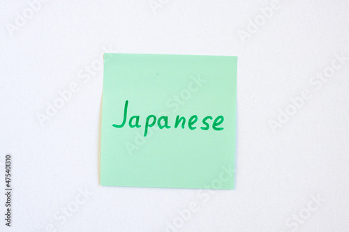 Top view flat lay of the reminder notepaper of green color with word Japanese on it on white background. Flashcards and language studies concept