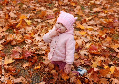 Child girl sitting on fallen leaves in autumn city park. Beautiful nature  trees with yellow leaves.