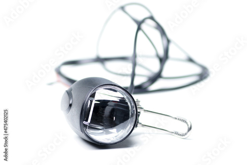 Bicycle headlight with mirrored lens. The flashlight for the electric bike lies on a white background. Bicycle headlight with black blurred cable.