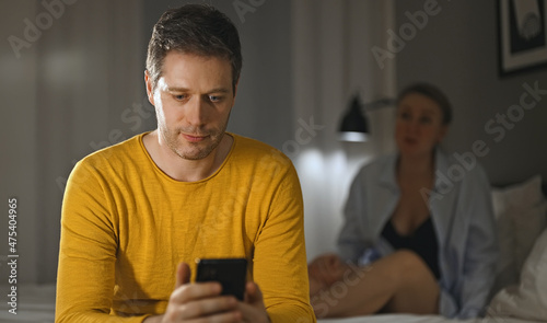 Phone addiction concept. Man with smartphone, upset woman on background.