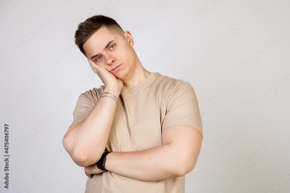 Young handsome guy holding his head with his hand, tired after a long and hard working day, standing on a white background looking at the camera Young handsome guy holding his head with his hand, tired after a long and hard working day, standing on a white background looking at the camera
